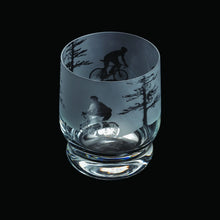 Clear glass tumbler with engraved design of a cyclist and trees on a black background