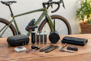 Velo-Tool repair accessories laid out on a wooden table in front of a green gravel bike: CO2 pump, cartridges, tubeless kit, tyre levers and multitool bits