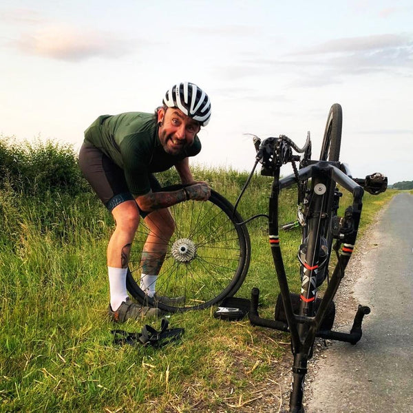 Cyclist changing inner tube on the side of the road during a bicycle ride. He's using Velo-Tool repair kit to do it.