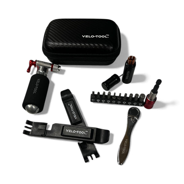 Velo-Tool bicycle repair kit with multiple black tools, a carbon-fiber-textured black carrying case, and a small red accent tool, arranged on a white background.