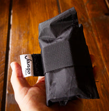 Black pouch held in a hand with a visible brand label on a wooden surface