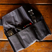 Black tool roll with tools on a wooden surface