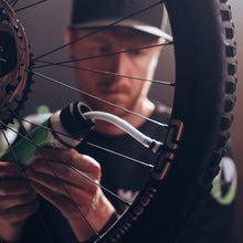 Person working on a bicycle wheel inserting oko magic milk  high fibre tubeless tyre sealant with a blurred background