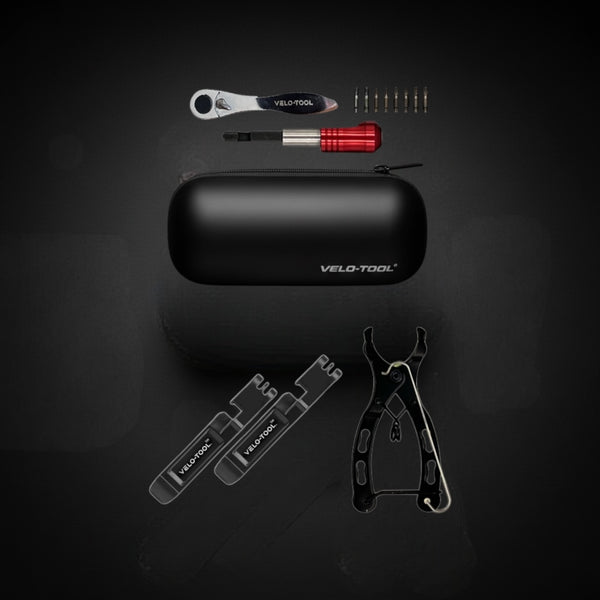 Collection of bicycle tools including a black tool case, wrenches, and other tools on a dark background.