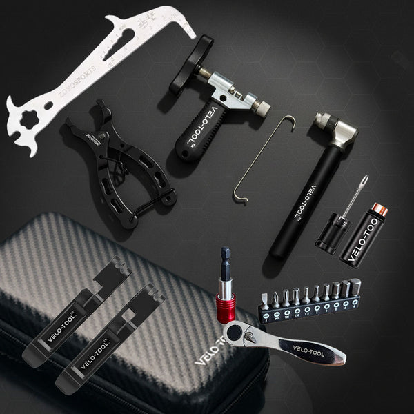 A VeloTool bicycle tool kit arranged on a dark surface, including a carbon-fiber zip case, multiple black and silver tools, a small screwdriver, and a set of bit holders. The tools are branded with the VeloTool name.